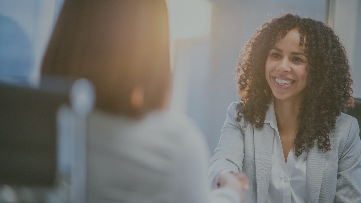 A client meeting, with a smiling woman shaking hands across the desk
