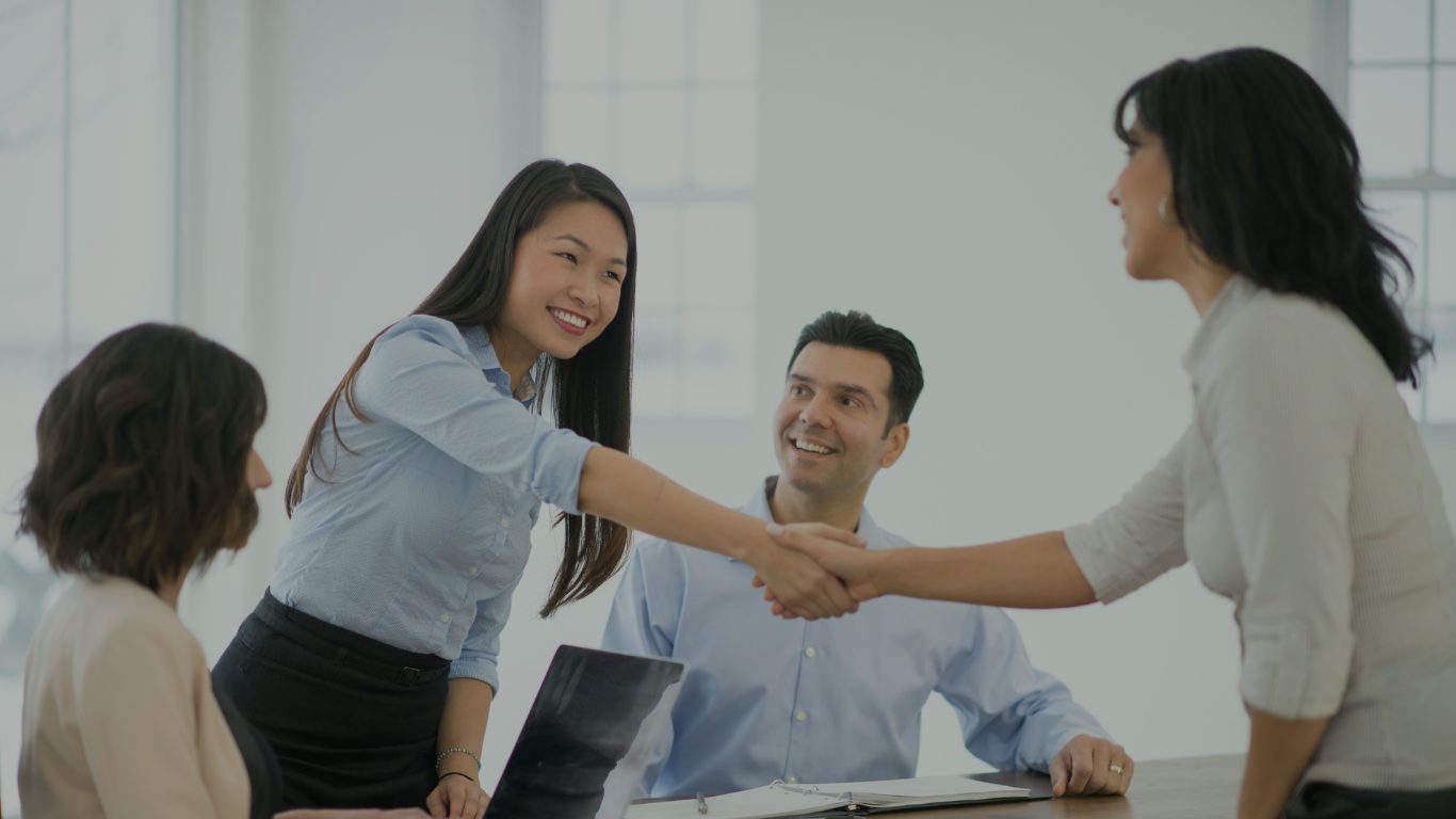 A commercial team meeting, with two colleagues shaking hands across the table
